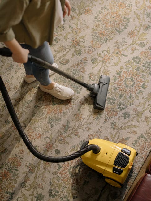 A professional cleaner, dressed in full white protective gear including a suit, gloves, face mask, and shoe covers, is performing deep carpet cleaning at a residential property. The person is using a 